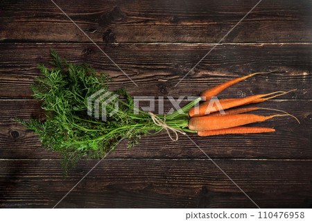Top down view, bunch of fresh carrot roots with green leaves, holding together with rope cord, on dark wooden board 110476958
