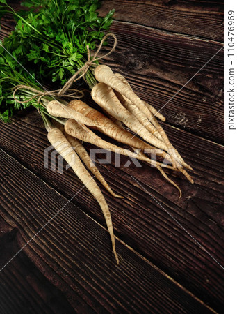 Bunch of parsnips with green leaves on dark wooden desk. Bunch of parsnips with green leaves on dark wooden desk. 110476969