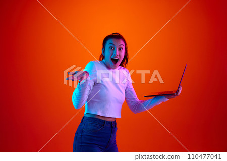 Wow. Shocked, surprised woman looking at camera widely open mouth and holding laptop against gradient studio background. 110477041