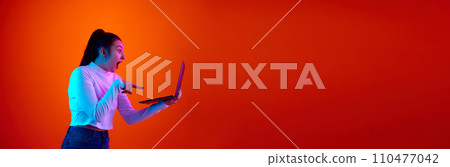 Banner. Side view portrait of woman pointing to laptop and widely opening mouth shouting against gradient background with negative space to insert text. 110477042