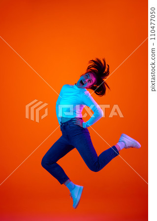 Full length portrait of young overjoyed woman jump high of joy and happiness against gradient pink-orange background in neon light. Full length portrait of young overjoyed woman jump high of joy and happiness against gradient pink-orange background in neon light. 110477050
