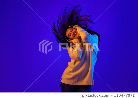 Elevated Energy. Dynamic portrait of girl in headphones energetically shakes her head to rhythm of music and her hair develops in movement. Elevated Energy. Dynamic portrait of girl in headphones energetically shakes her head to rhythm of music and her hair develops in movement. 110477071