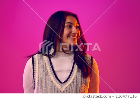 Portrait of young woman with long brunette hair, dressed casual outfit smiling looking away against gradient pink background. Beauty. 110477136
