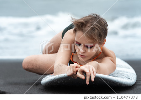 Close-up view of woman surfer lying on surfboard with eyes closed, looks so relaxed and peaceful 110477378