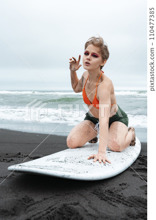 Sensuality woman surfer strikes pose on knees atop surfboard. Sports fashion model looking at camera 110477385
