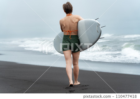 Rear view unrecognizable female surfer walking beach carrying surfboard on background of sea waves Rear view unrecognizable female surfer walking beach carrying surfboard on background of sea waves 110477418