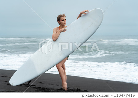 Female sports fashion model holding surfboard and standing behind it, concept of active lifestyle 110477419