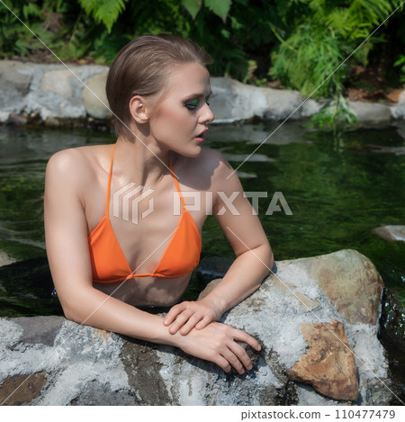 Slim adult woman with blonde hair is relaxing in pool with natural geothermal water and sunbathing Slim adult woman with blonde hair is relaxing in pool with natural geothermal water and sunbathing 110477479