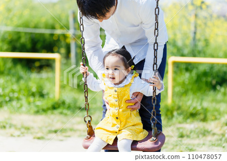 Cute little girl and her dad playing on the swing in the park Cute little girl and her dad playing on the swing in the park 110478057