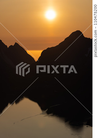 Golden midnight sun silhouettes Reinebringen, mirrored in Lofoten's calm waters Golden midnight sun silhouettes Reinebringen, mirrored in Lofoten's calm waters 110478200
