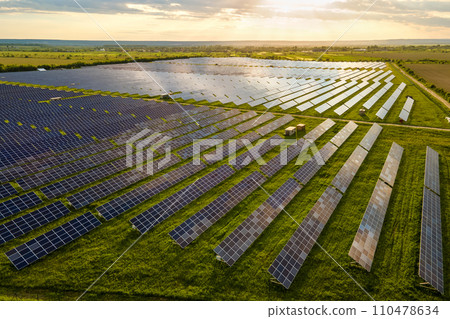 Aerial view of large sustainable electrical power plant with many rows of solar photovoltaic panels for clean ecological electric energy at sunrise. Renewable electricity with zero emission concept. Aerial view of large sustainable electrical power plant with many rows of solar photovoltaic panels for clean ecological electric energy at sunrise. Renewable electricity with zero emission concept. 110478634