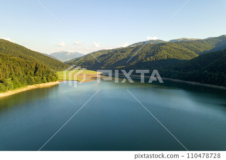 Aerial view of big lake with clear blue water between high mountain hills covered with dense evergreen forest. Aerial view of big lake with clear blue water between high mountain hills covered with dense evergreen forest. 110478728