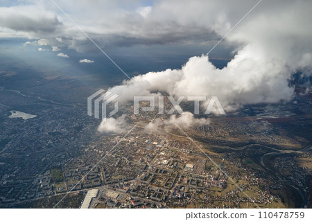 Aerial view from airplane window at high altitude of distant city covered with white puffy cumulus clouds 110478759
