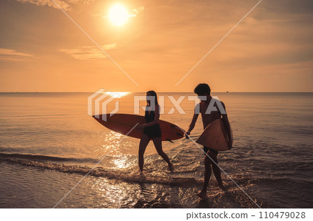 Asian couple holding surfboard on the beach at morning 110479028