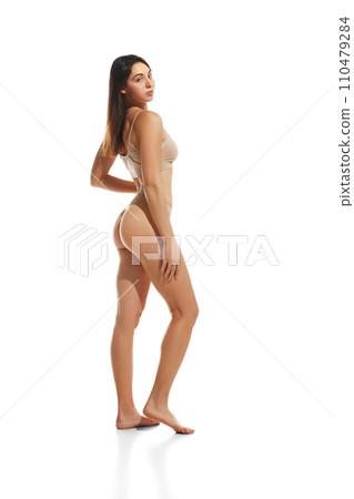 Side view full-length image of young attractive woman with slim, fit, smooth body standing in underwear against white studio background 110479284