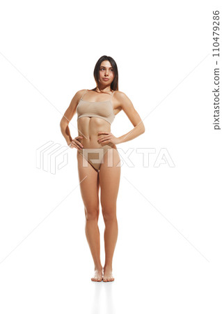 Comfortable lingerie. Young beautiful woman with slim body wearing cotton beige underwear against white studio background Comfortable lingerie. Young beautiful woman with slim body wearing cotton beige underwear against white studio background 110479286