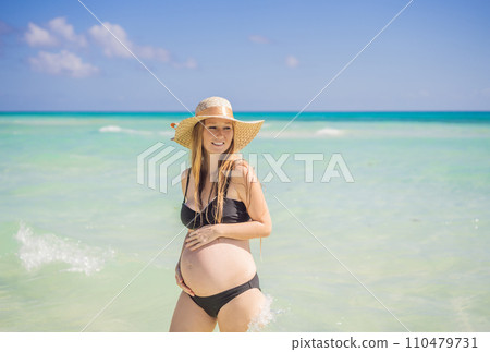 Radiant and expecting, a pregnant woman stands on a pristine snow-white tropical beach, celebrating the miracle of life against a backdrop of natural beauty Radiant and expecting, a pregnant woman stands on a pristine snow-white tropical beach, celebrating the miracle of life against a backdrop of natural beauty 110479731