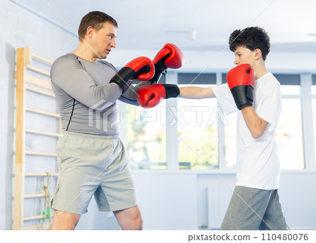 Middle-aged man and teenage boy training boxing during sports classes 110480076