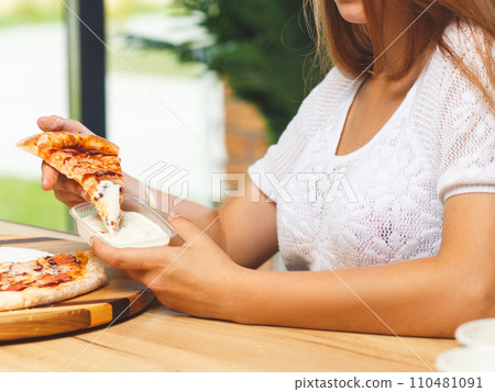 A girl dips a slice of pizza in sauce 110481091