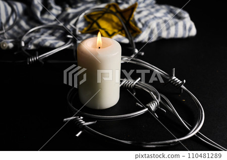 Holocaust memory day. Arbed wire and burning candle on black background 110481289