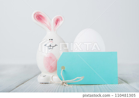 Happy Easter greeting card. Miniature wooden house. Rabbits, colorful eggs, spring flowers with tag for text 110481305