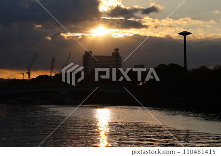 早晨的城市景觀，有雲、橘色的日出天空、輪廓建築等，以及水面上有太陽路徑的河流 110481415