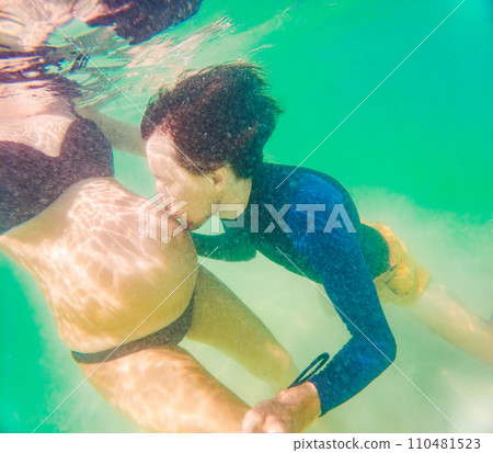 Amidst the tranquil turquoise sea, a pregnant woman and her husband share a serene moment, celebrating the beauty of impending parenthood in the gentle waves 110481523