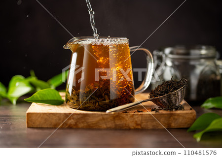Fresh hot tea in a glass tea pot and dry loose leaves, dark moody background Fresh hot tea in a glass tea pot and dry loose leaves, dark moody background 110481576