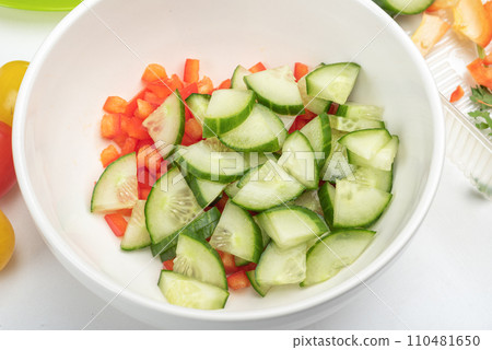 Bowl with pieces of sweet pepper and cucumber for preparing salad. Bowl with pieces of sweet pepper and cucumber for preparing salad. 110481650