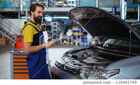 Portrait of licensed technician in auto repair shop doing car routine checkup using tablet, looking for damages. Certified mechanic in garage checking to see if vehicle components need to be changed Portrait of licensed technician in auto repair shop doing car routine checkup using tablet, looking for damages. Certified mechanic in garage checking to see if vehicle components need to be changed 110481749