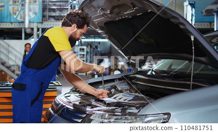 Trained technician in auto repair shop using virtual reality goggles to visualize car components in order to fix them. Man wearing modern vr headset while working on busted vehicle Trained technician in auto repair shop using virtual reality goggles to visualize car components in order to fix them. Man wearing modern vr headset while working on busted vehicle 110481751