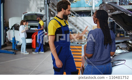 Teamworking colleagues in garage workspace fixing car for customers, thoroughly checking underneath vehicle hood. Mechanics doing routine maintenance on automobile in auto repair shop Teamworking colleagues in garage workspace fixing car for customers, thoroughly checking underneath vehicle hood. Mechanics doing routine maintenance on automobile in auto repair shop 110481752
