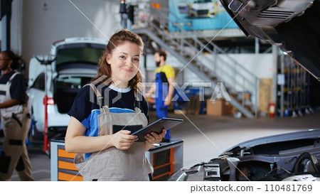 Portrait of smiling mechanic in repair shop using tablet to check car performance parameters during maintenance. Happy garage workplace employee using device to examine damaged vehicle Portrait of smiling mechanic in repair shop using tablet to check car performance parameters during maintenance. Happy garage workplace employee using device to examine damaged vehicle 110481769