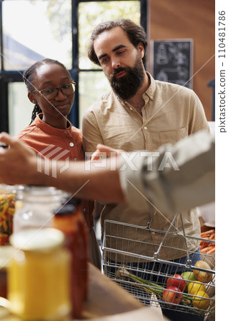 Close-up of caucasian boyfriend and African American girlfriend browsing through a section filled with fresh and natural merchandise. Interracial couple with a basket doing organic food shopping. Close-up of caucasian boyfriend and African American girlfriend browsing through a section filled with fresh and natural merchandise. Interracial couple with a basket doing organic food shopping. 110481786