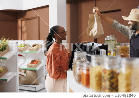 Male vendor hands delivery lady takeaway paper bag. African american woman courier delivers eco friendly natural products to clients after picking up orders at the local convenience store. Male vendor hands delivery lady takeaway paper bag. African american woman courier delivers eco friendly natural products to clients after picking up orders at the local convenience store. 110481840
