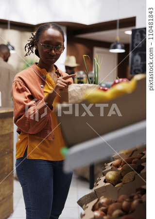 Black woman doing eco friendly shopping at the local grocery store. Buying fresh, locally grown, organic produce in reusable bags. Zero waste, sustainability, and conservation focus. Black woman doing eco friendly shopping at the local grocery store. Buying fresh, locally grown, organic produce in reusable bags. Zero waste, sustainability, and conservation focus. 110481843