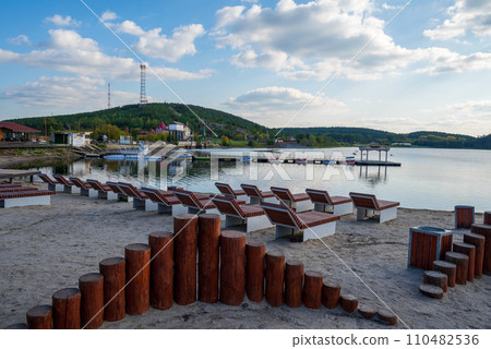 sandy beach with sun beds on the background of a pier, boats and mountains 110482536
