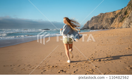 Smiling young woman running on sandy sea beach on 110482562