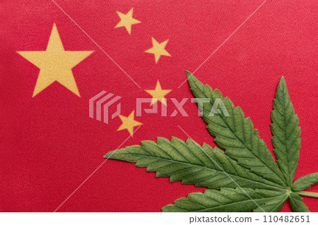 Big flag of PRC close up and fresh cannabis leaf. Illegal cultivation and distribution. Medical use Big flag of PRC close up and fresh cannabis leaf. Illegal cultivation and distribution. Medical use 110482651