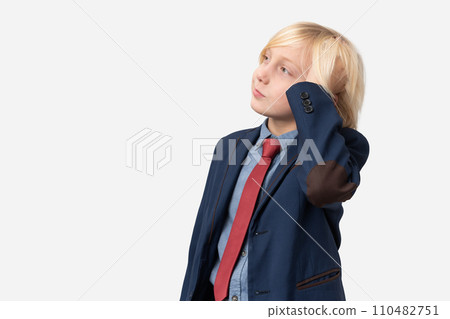 Thoughtful boy with blond hair dressed in blue shirt, red tie and blue jacket standing with hand on chin and looking away isolated over white background Thoughtful boy with blond hair dressed in blue shirt, red tie and blue jacket standing with hand on chin and looking away isolated over white background 110482751