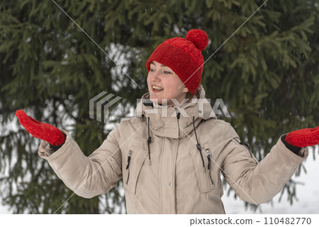 Happy smiling girl in warm winter clothes standing among spruce trees. Young woman enjoys nature of snowy forest 110482770