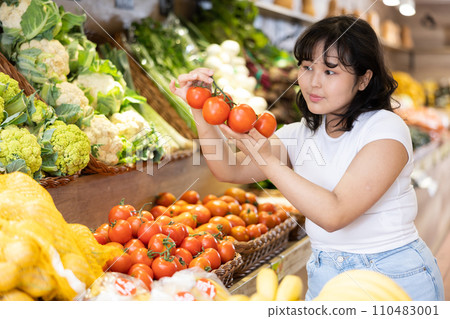 Delighted young woman purchaser choosing tomatoes in grocery store Delighted young woman purchaser choosing tomatoes in grocery store 110483001