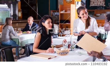 Polite young waitress helping with menu to African American Polite young waitress helping with menu to African American 110483192