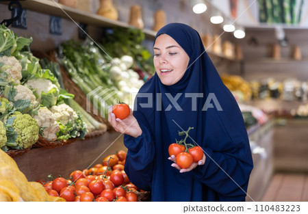 Woman in a veil buys ripe tomatoes in supermarket Woman in a veil buys ripe tomatoes in supermarket 110483223