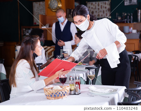 Waitress in protective mask helping woman in choosing meals from menu 110483248