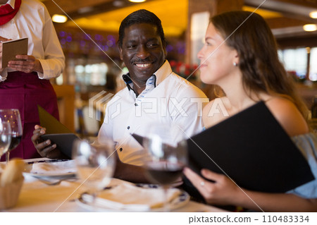 Positive female waiter writing down order from visitors in restaurant 110483334
