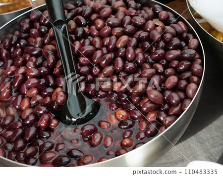 Pickled black olives scooped with skimmer out of container 110483335