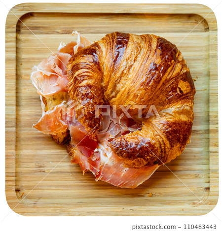 Simple snack is prepared on wooden board for visitor of cafe - large croissant with slices of ham 110483443