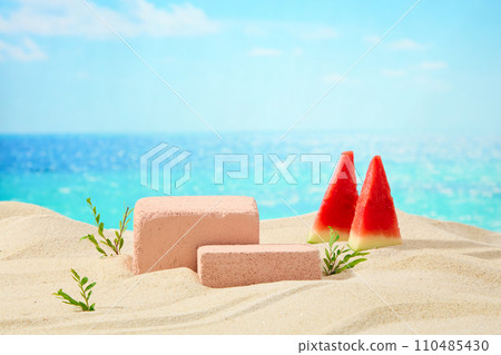 On the sand, pieces of succulent watermelon are decorated with bricks and grass. Behind is the sea and blue sky. Great vacation, space for product advertising 110485430