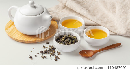 Tea cup, teapot and dried tea leave with spoon and napkin, tea set on table 110487091